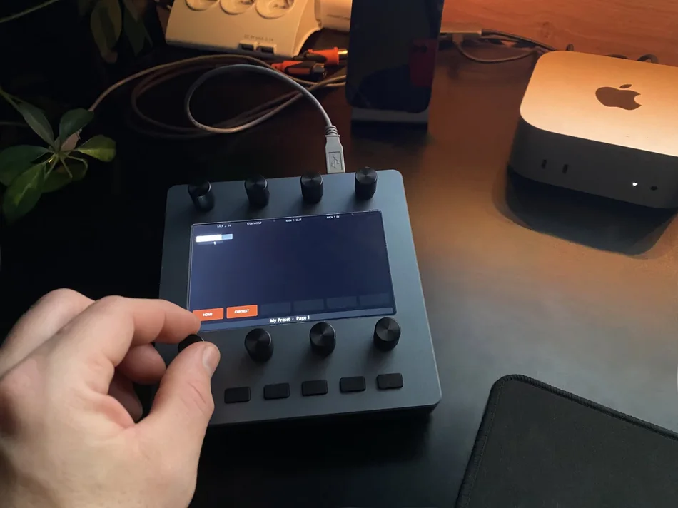 A hand turning one of the eight encoders on Electra One Mini, on a desk next to a Mac mini