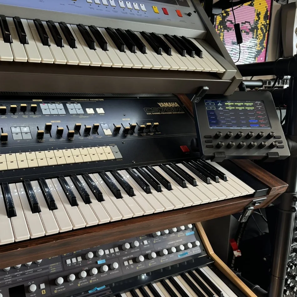An Electra One mk2 on a stand beside a Yamaha CS70M, in a rack of vintage synthesizers
