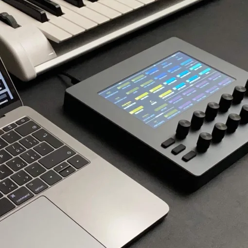An Electra One mk2 on a desk between a laptop and a synthesizer keyboard, its screen showing a page of parameters
