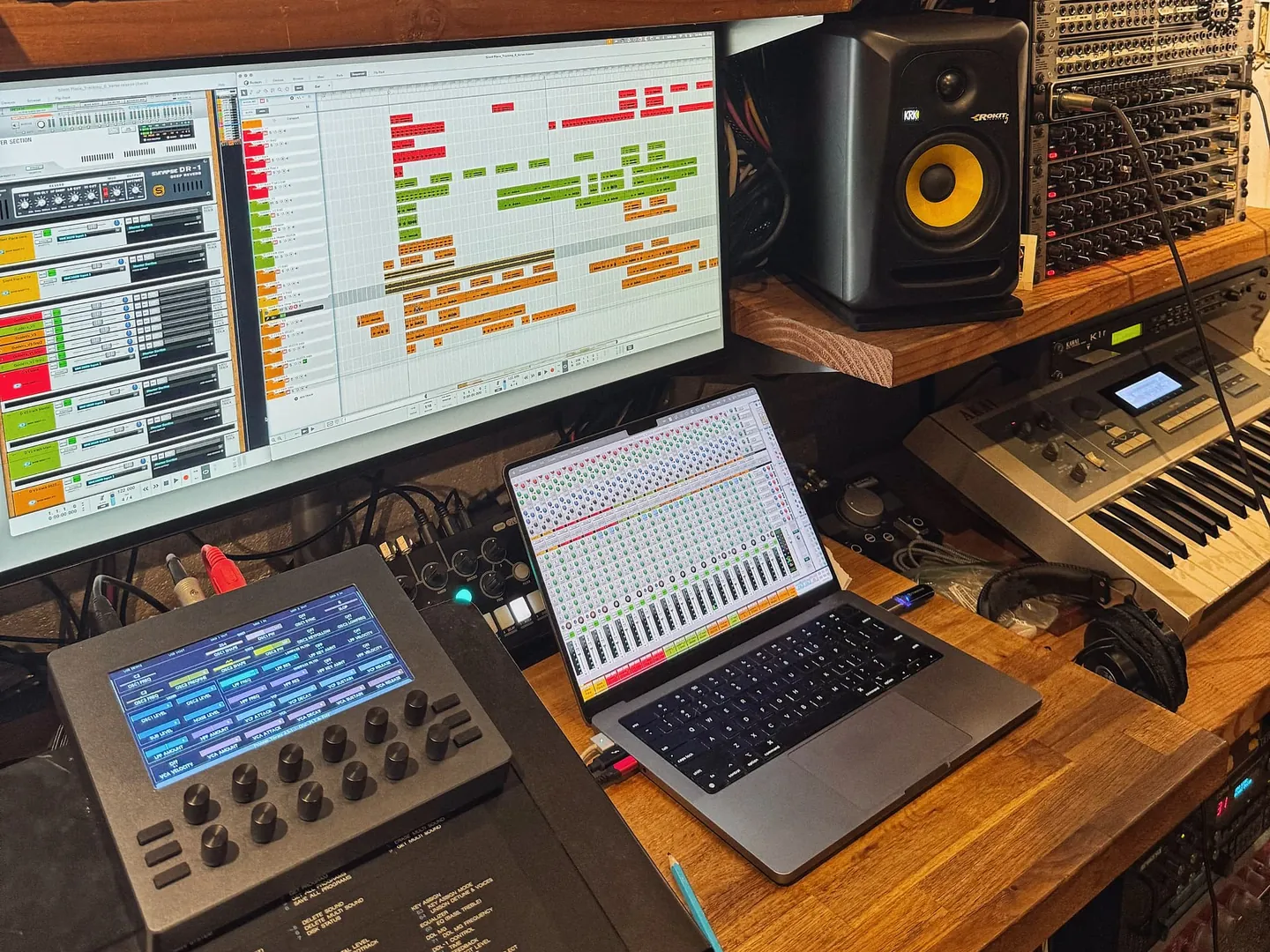 Electra One mk2 on a studio desk in front of a DAW screen and a laptop, its page of synthesizer parameters lit up